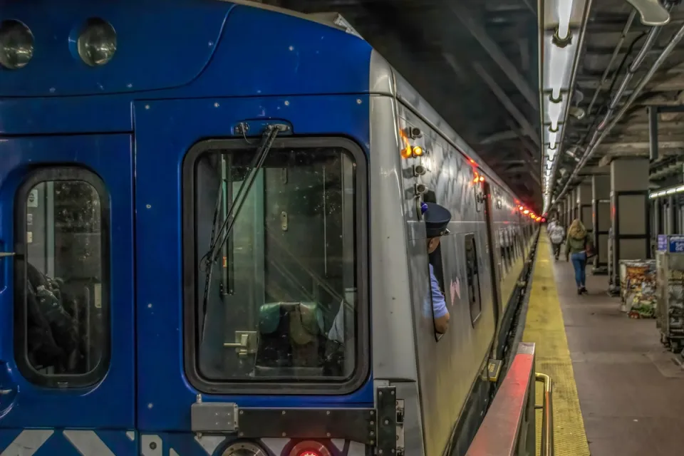 New York City subway train at station with operator looking back toward platform.